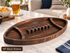 A football-shaped wooden serving tray made of dark black walnut wood, engraved with a buffalo bills logo and 'GO BILLS' text, displayed on a marble table in a living room setting.